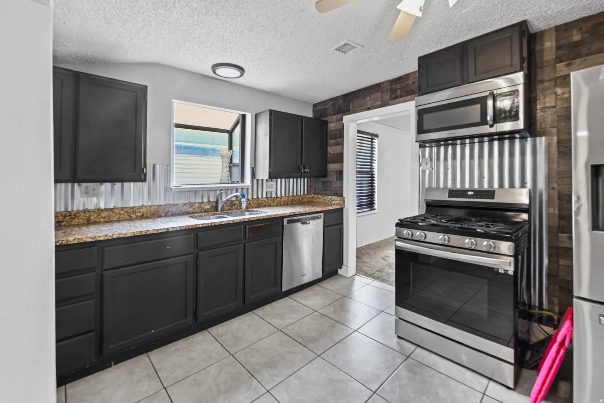 Kitchen with stainless steel appliances, a textured ceiling, a ceiling fan, light stone counters, and light tile patterned floors