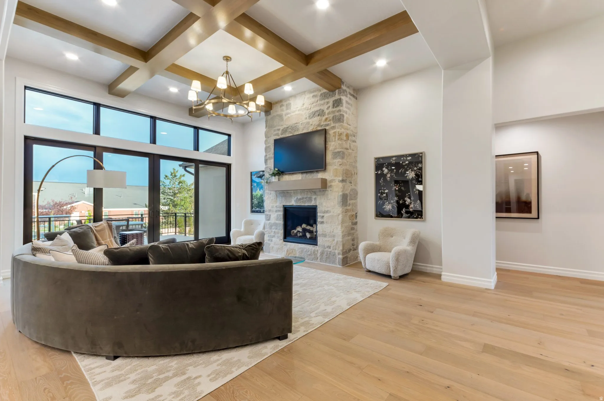 Living area with light wood-type flooring, suspended lighting, coffered ceiling, and a stone fireplace
