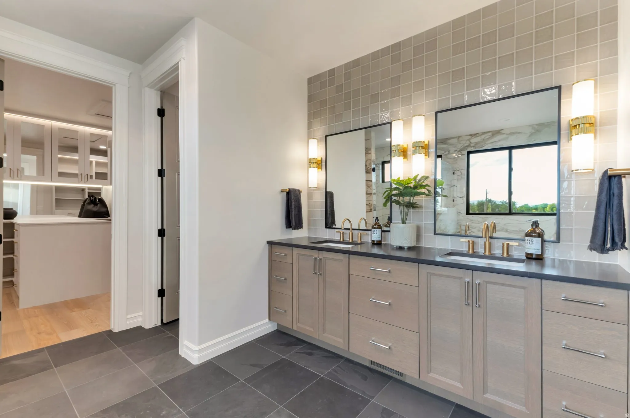 Bathroom featuring double vanity, tasteful backsplash, a walk in closet, dark tile patterned floors, and a shower with shower door