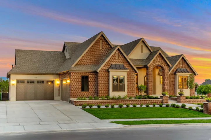 View of front of house with a front yard, brick siding, roof with shingles, a garage, and driveway