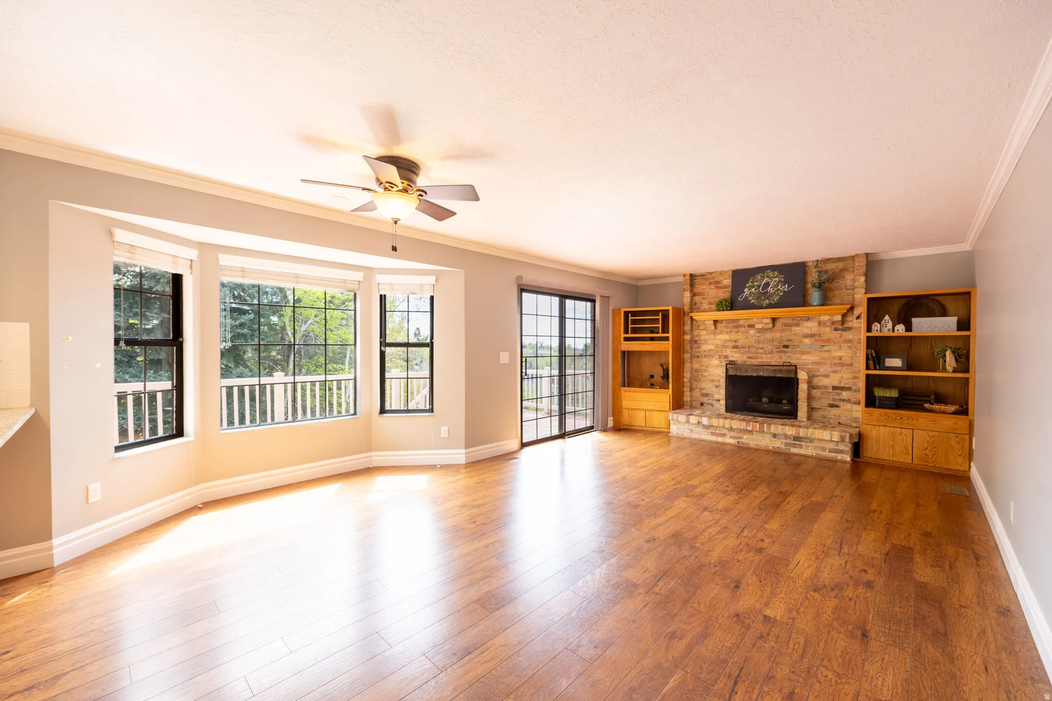 Brick surround fireplace in family room with hardwood flooring, deck access and views through the bay window.