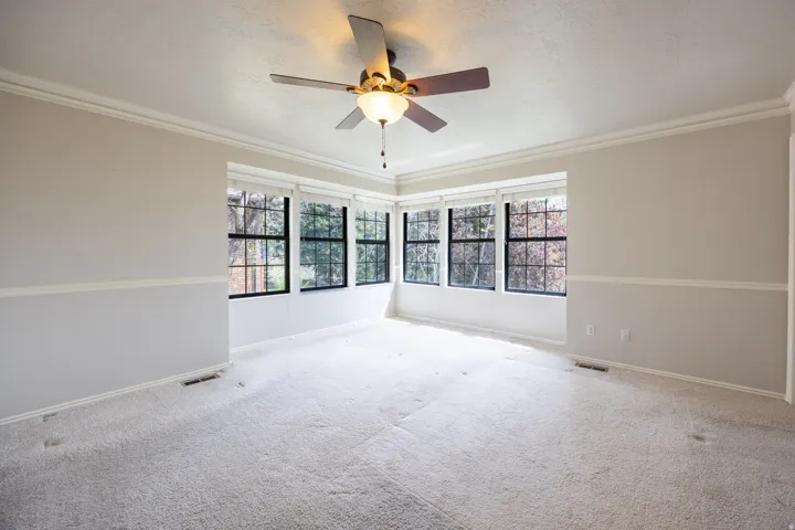 Primary bedroom with corner window set, crown moulding and ceiling fan.