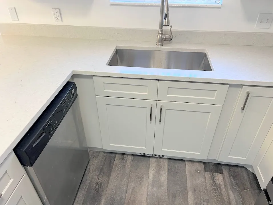 Kitchen view of dishwasher, light stone counters, white cabinetry, and dark wood finished floors