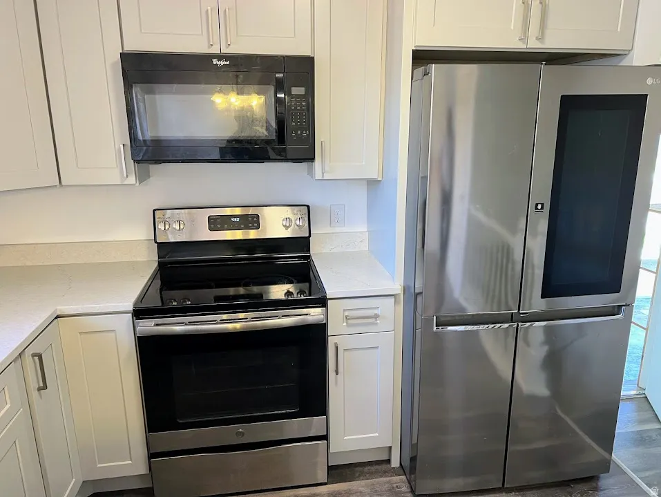 Kitchen with stainless steel appliances, white cabinetry, light stone countertops, and dark wood finished floors