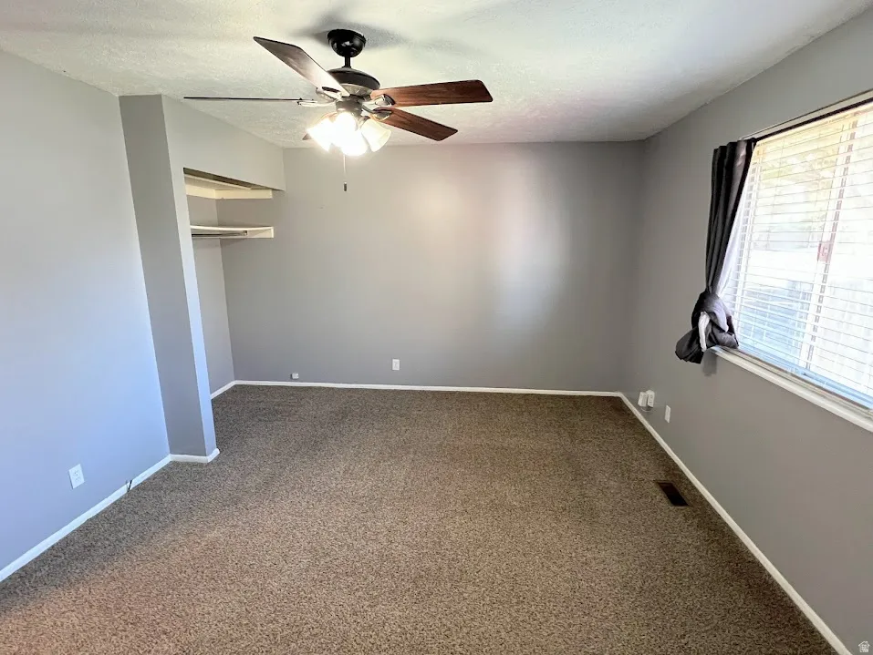 Unfurnished bedroom with a closet, dark colored carpet, a textured ceiling, and a ceiling fan