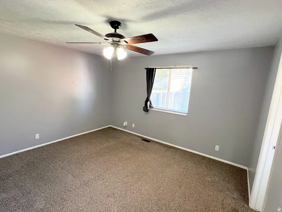 Unfurnished room with ceiling fan, dark colored carpet, and a textured ceiling