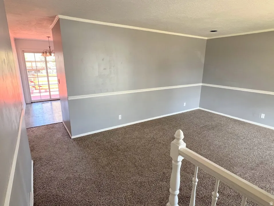 Unfurnished room featuring dark colored carpet, hanging lights, a textured ceiling, and crown molding