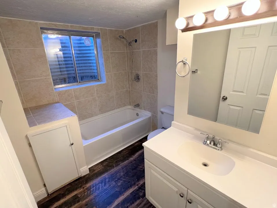 Bathroom with vanity, shower / bathtub combination, dark wood-style floors, and a textured ceiling
