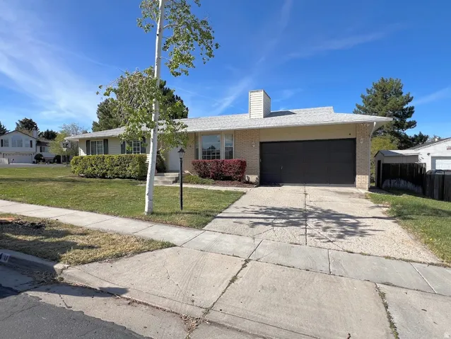 Ranch-style house with driveway, an attached garage, brick siding, a front lawn, and a chimney