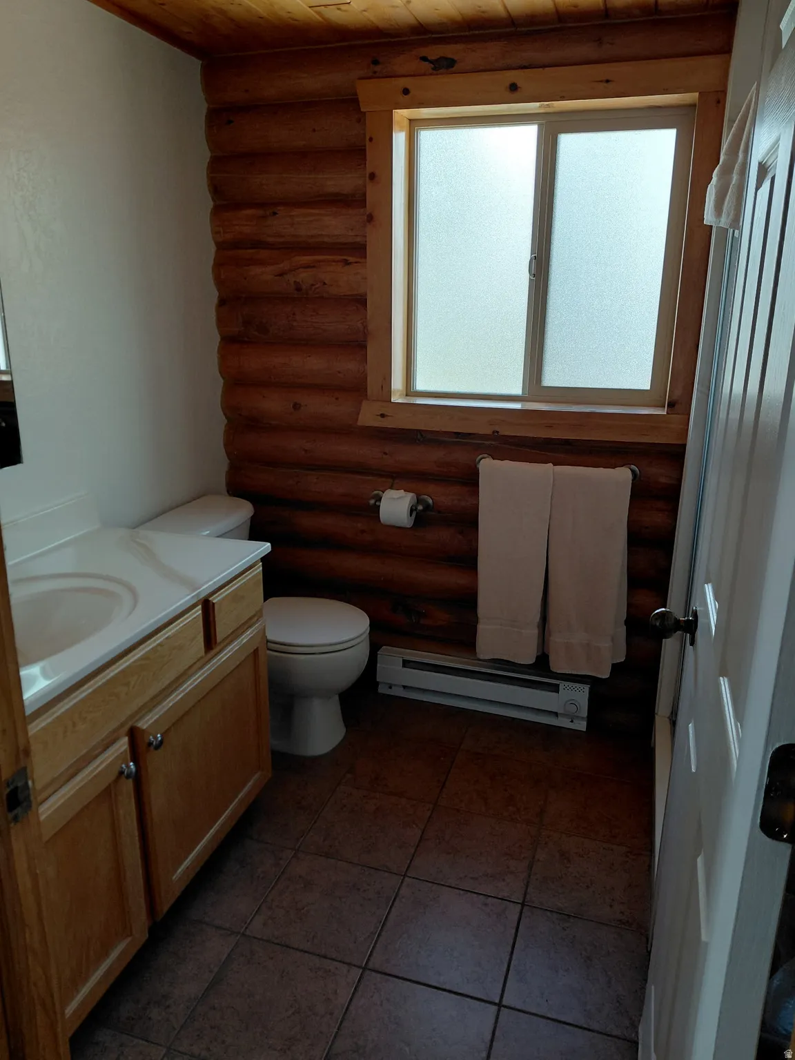 Bathroom featuring vanity, log walls, a baseboard heating unit, wood ceiling, and dark tile patterned flooring