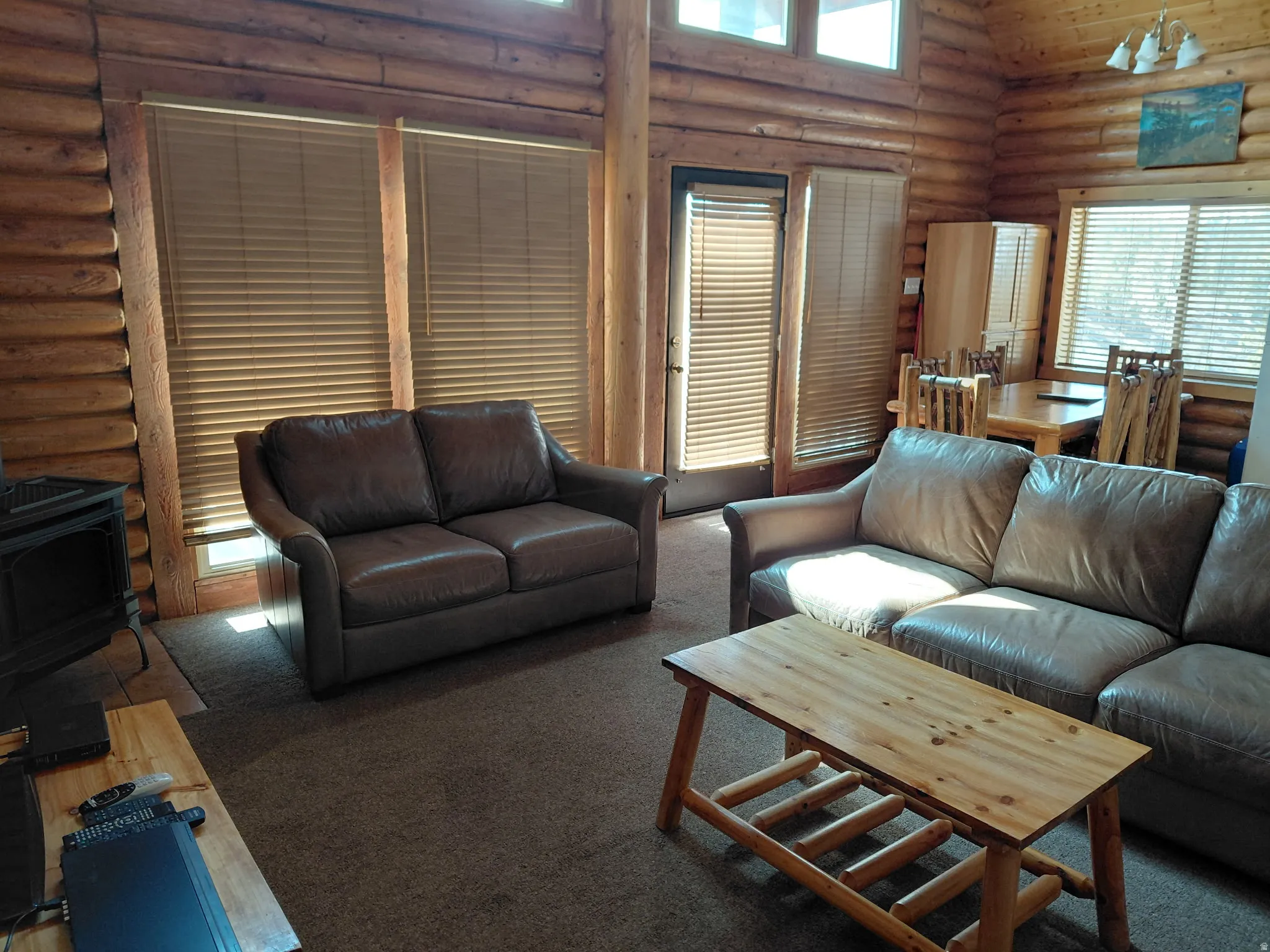 Living area featuring log walls, a wood stove, healthy amount of natural light, carpet, and vaulted ceiling