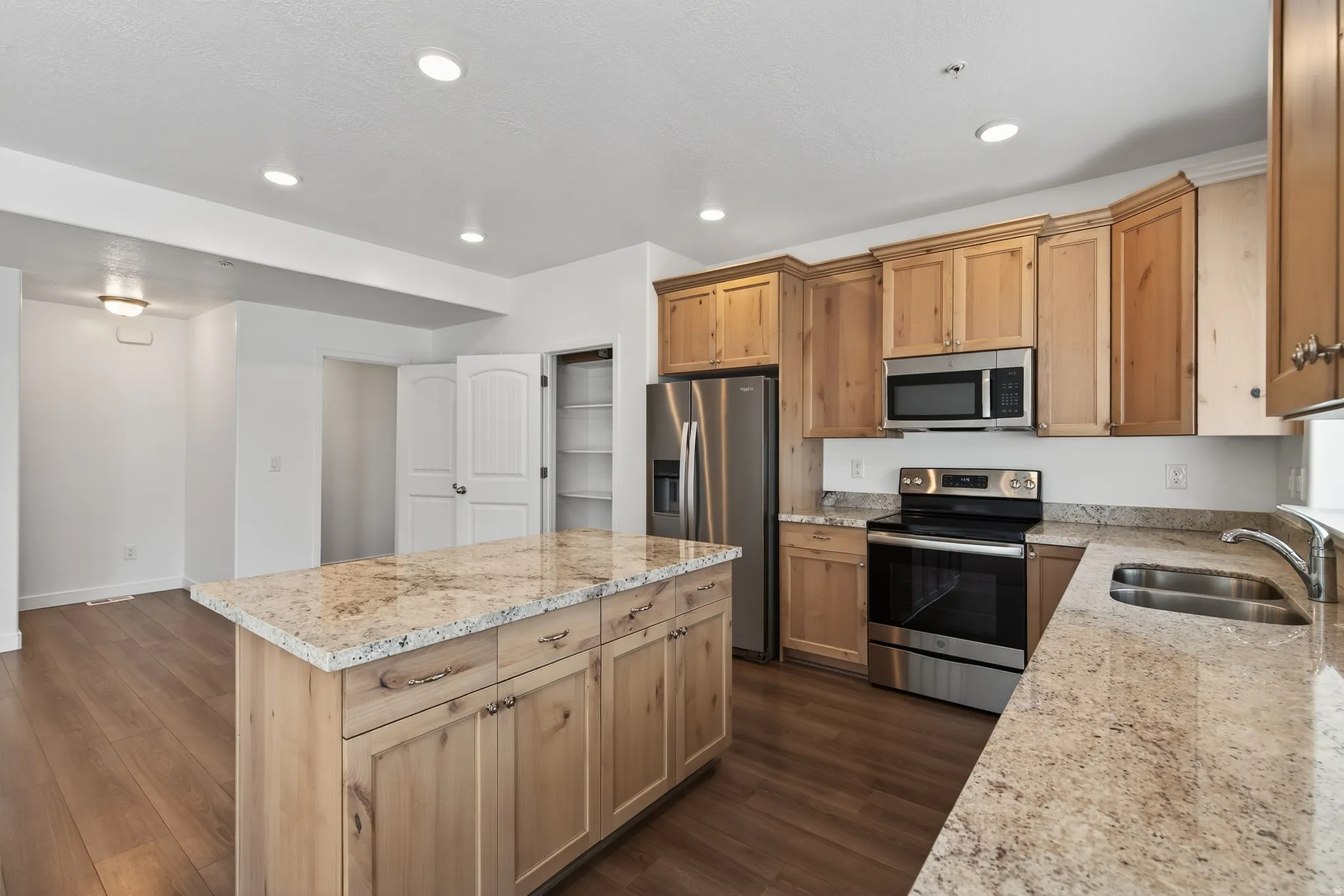 Kitchen featuring stainless steel appliances, a center island, light stone countertops, light wood finish cabinets, and dark wood-style floors
