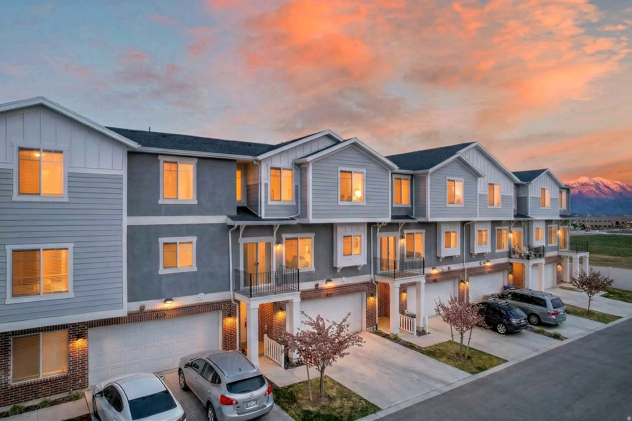 View of front of property with a balcony, board and batten siding, an attached garage, driveway, and brick siding