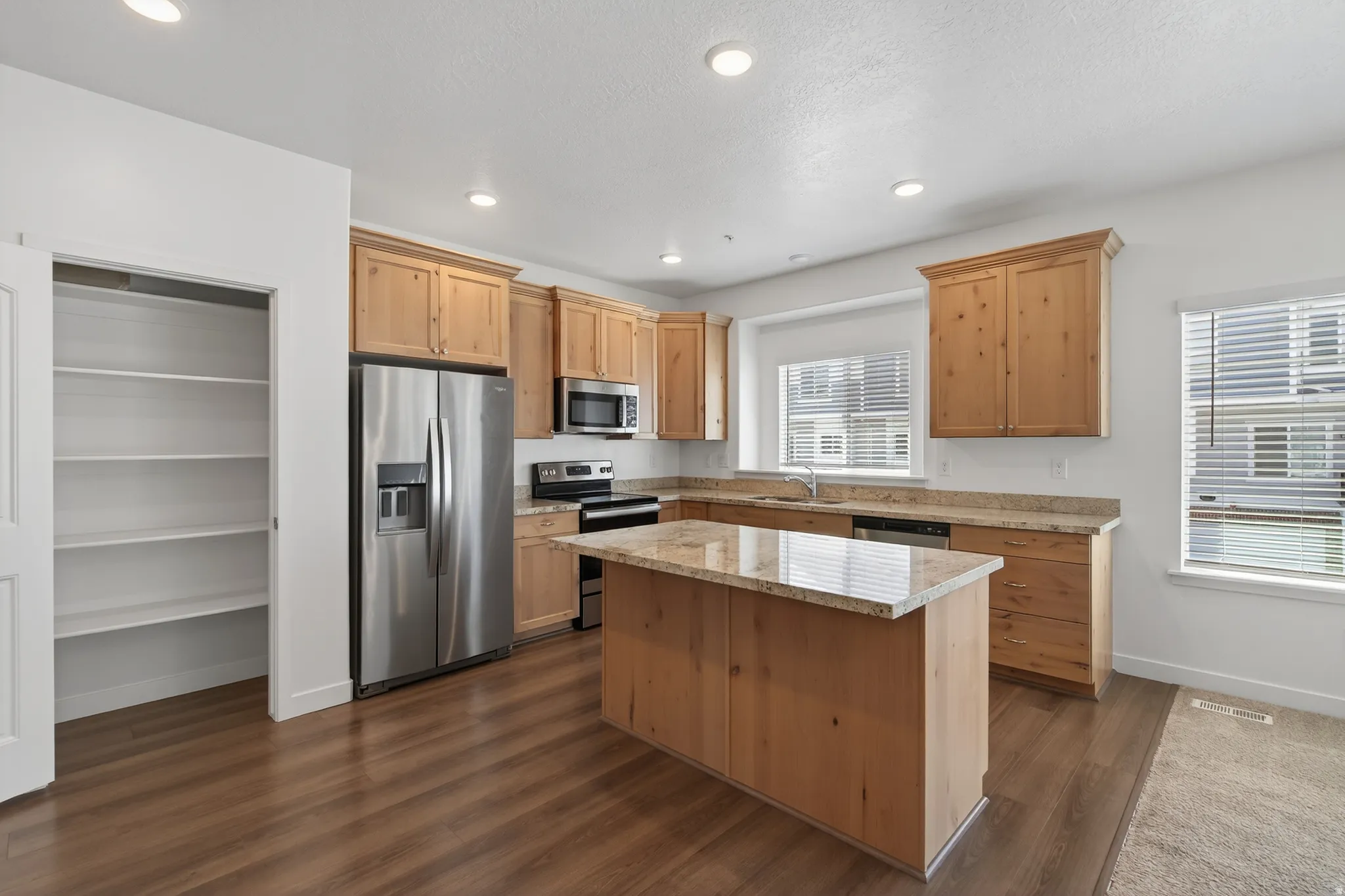 Kitchen featuring stainless steel appliances, a center island, light stone counters, dark wood finished floors, and recessed lighting