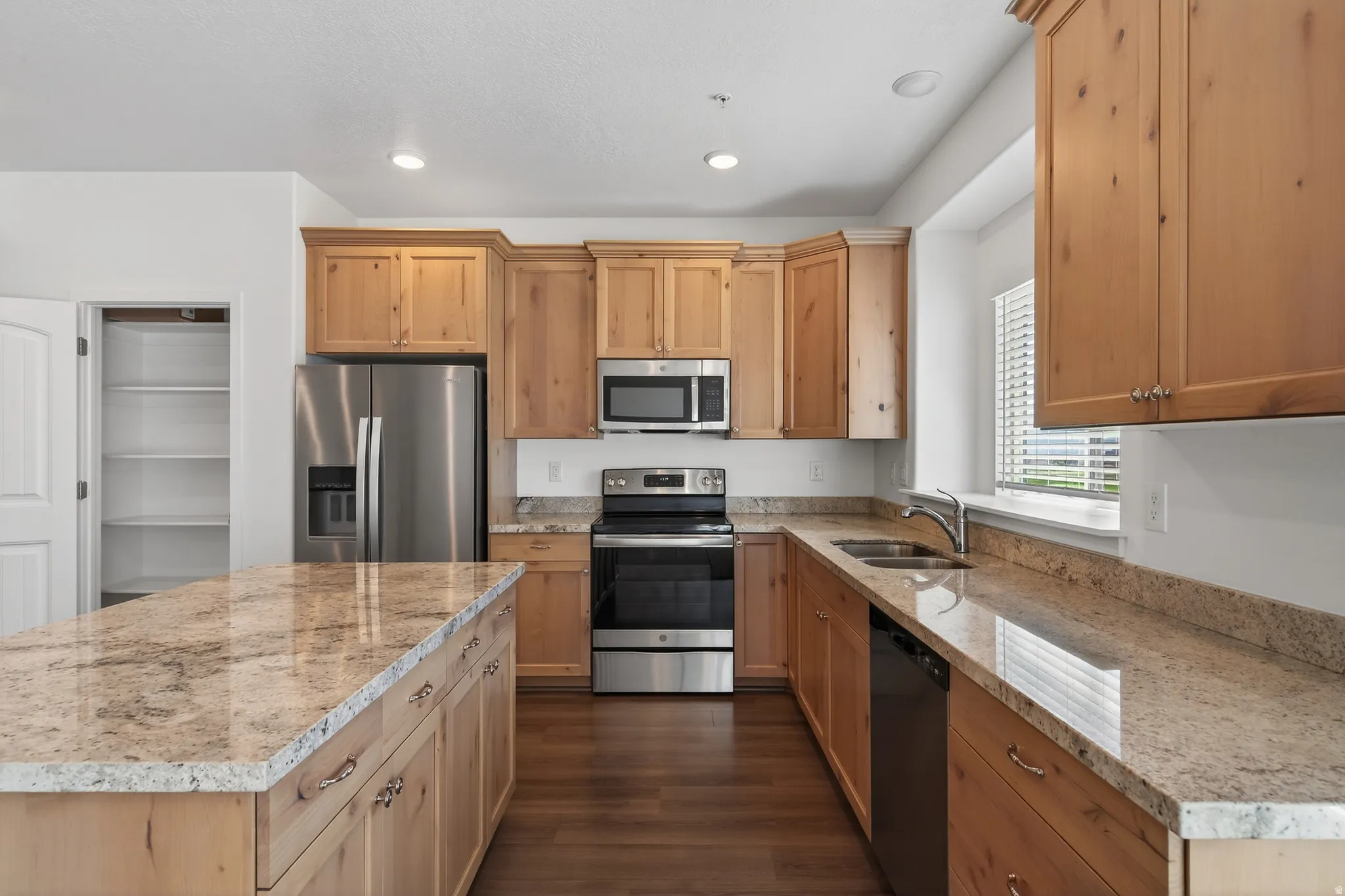 Kitchen featuring stainless steel appliances, light stone counters, recessed lighting, dark wood-style floors, and a center island