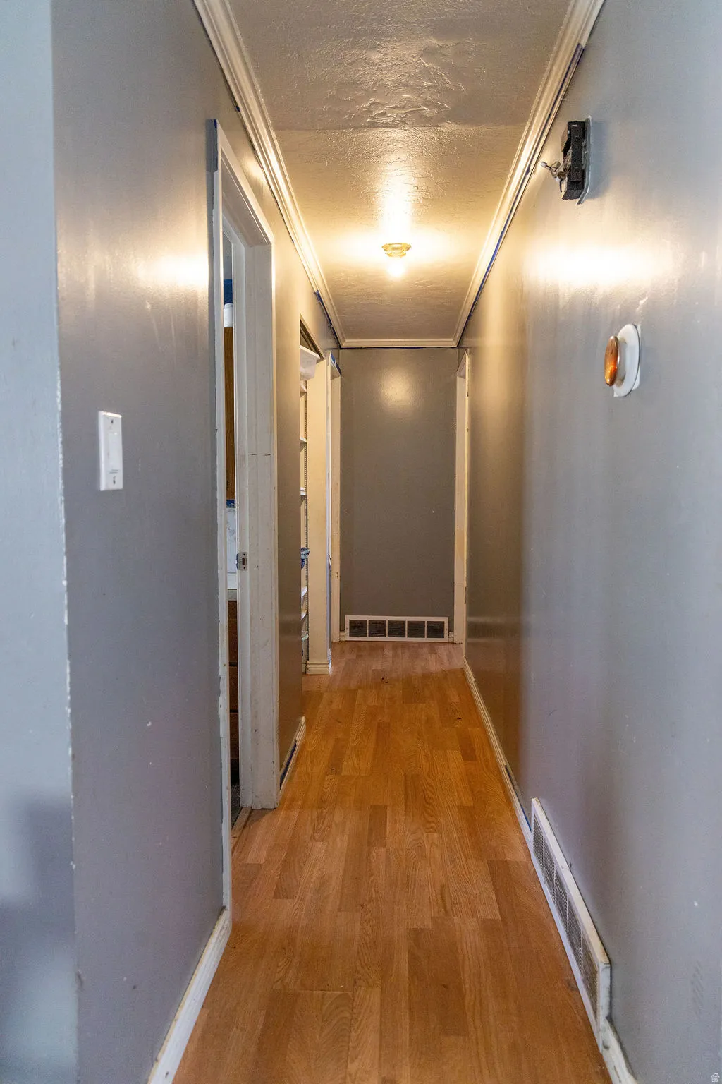 Corridor with a textured ceiling, light wood-style floors, and crown molding