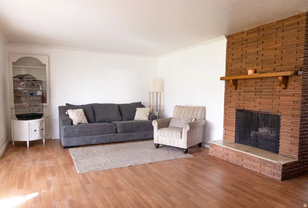 Living room with light wood finished floors, ornamental molding, and a brick fireplace