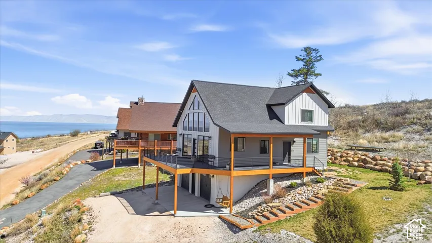 View of front of house with a deck with mountain view, an attached garage, driveway, roof with shingles, and a patio area