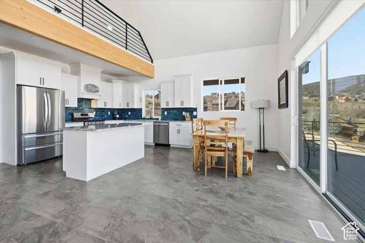 Kitchen with stainless steel appliances, light stone counters, white cabinets, a center island, and decorative backsplash