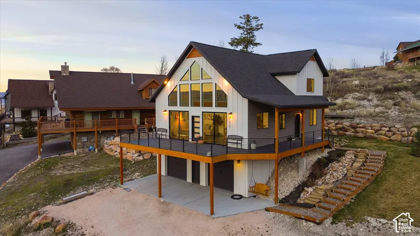 Back of property with a wooden deck, a patio area, driveway, and an attached garage