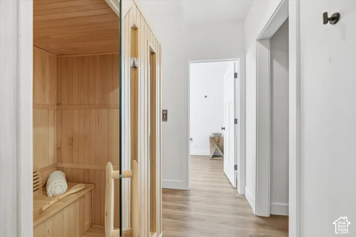 Hallway with a sauna, light wood-style flooring, and wood walls