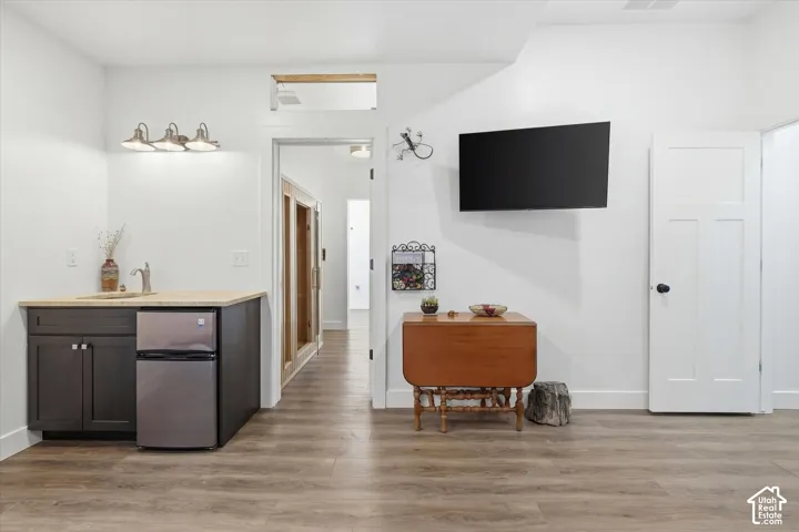 Flex Room/Bedroom/Exercise Room with wet bar, freestanding refrigerator, light finished floors, dark wood finish cabinetry, and light stone countertops
