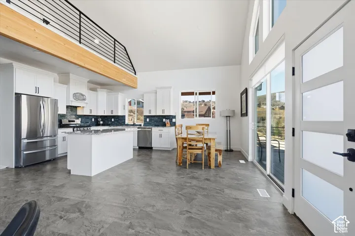 Kitchen featuring stainless steel appliances, decorative backsplash, white cabinets, a high ceiling, and healthy amount of natural light