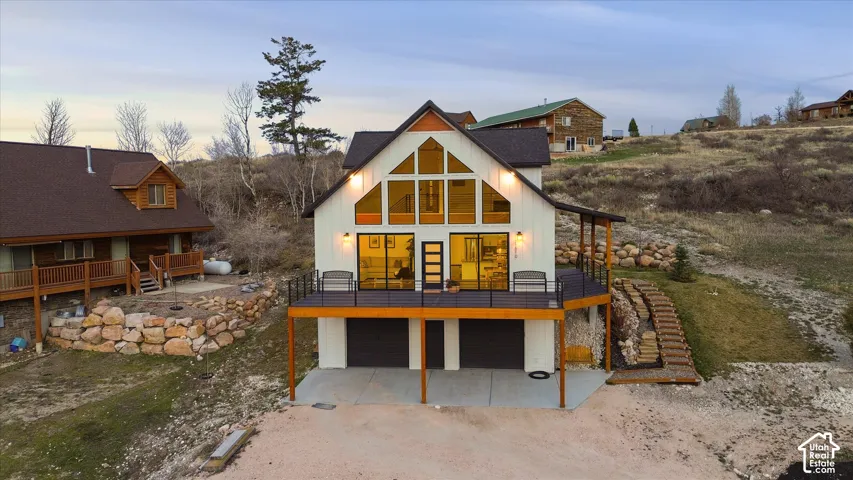 Back of house at dusk featuring a wooden deck, driveway, a garage, and a patio