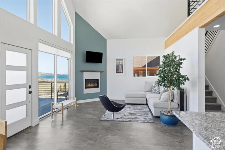 Living area featuring a high ceiling, a lit fireplace, and finished concrete flooring