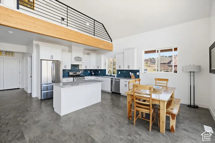Kitchen featuring stainless steel appliances, light stone counters, white cabinetry, a kitchen island, and backsplash