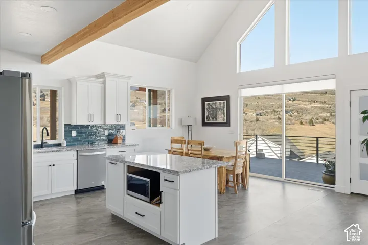 Kitchen with backsplash, stainless steel appliances, white cabinets, a kitchen island, and light stone counters