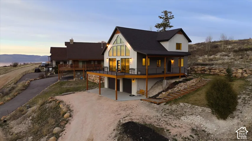 Back of property at dusk featuring dirt driveway, a patio area, a garage, and a deck with mountain view