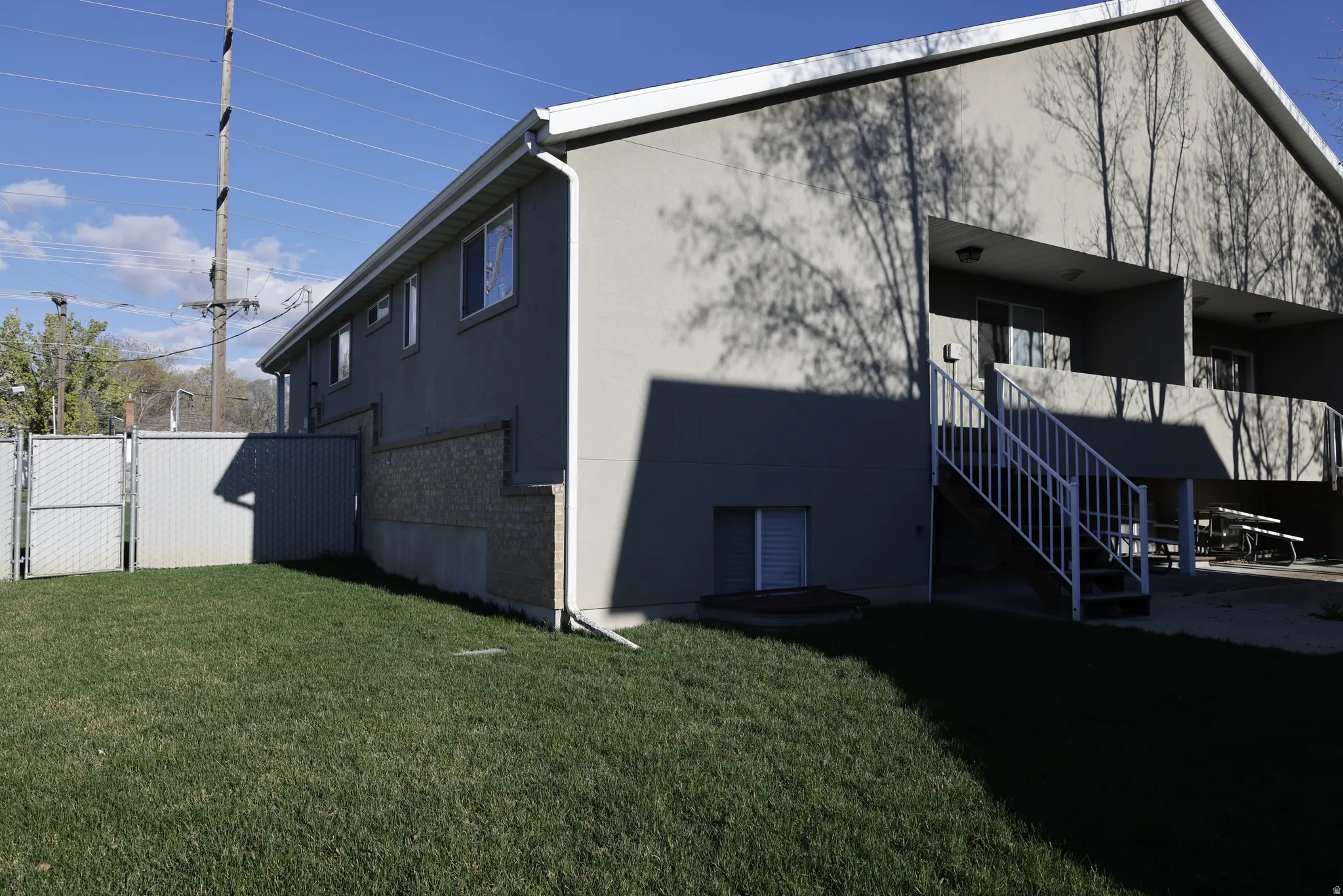 View of side of home featuring a lawn, brick siding, a patio area, and a gate