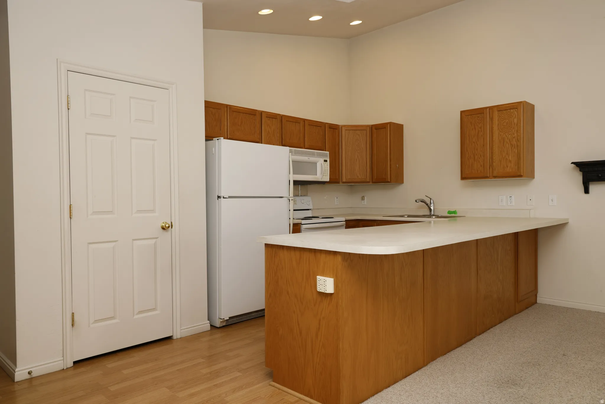 Kitchen with white appliances, a peninsula, light countertops, wood finish cabinetry, and recessed lighting