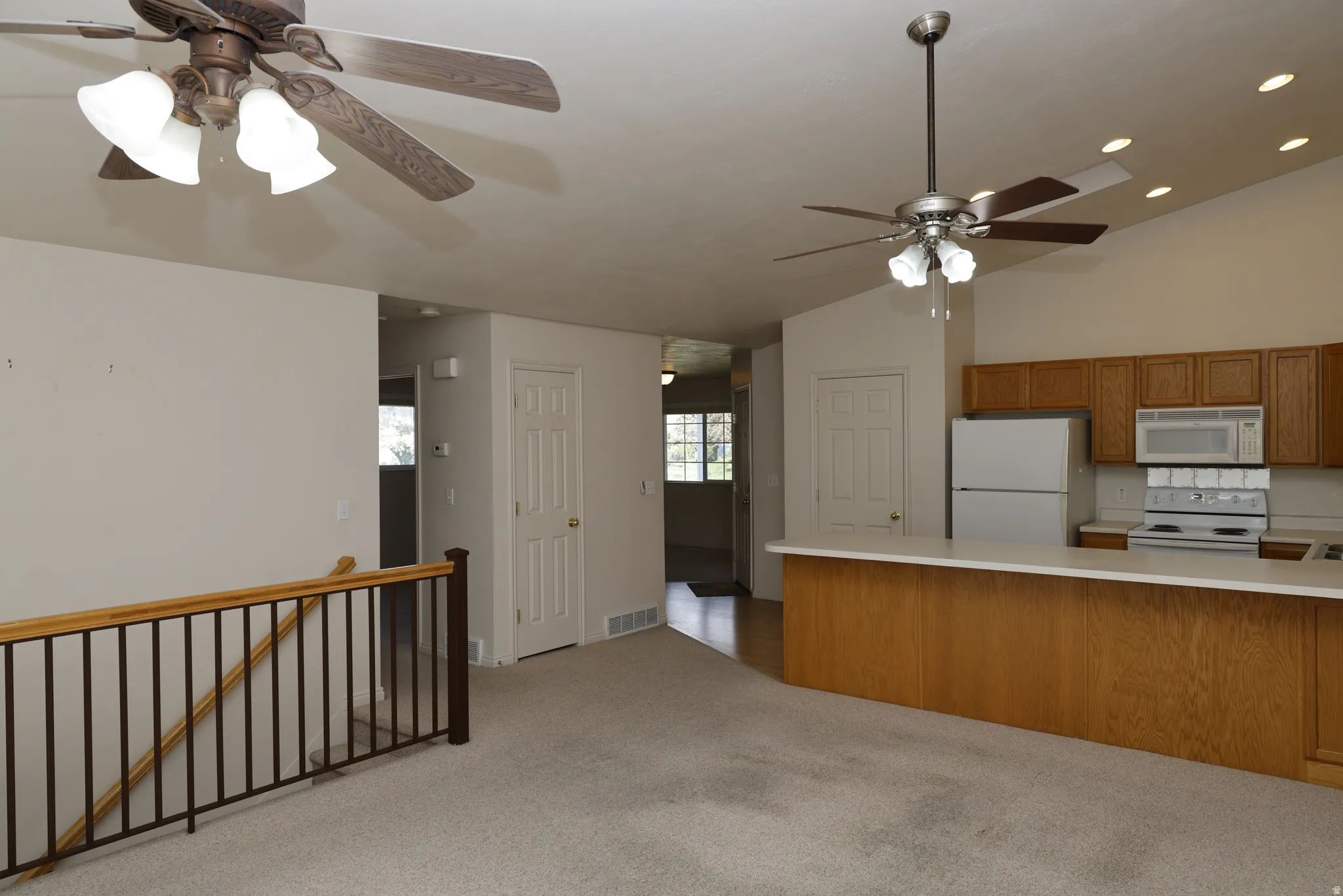 Kitchen with a ceiling fan, light countertops, wood finish cabinets, white appliances, and vaulted ceiling