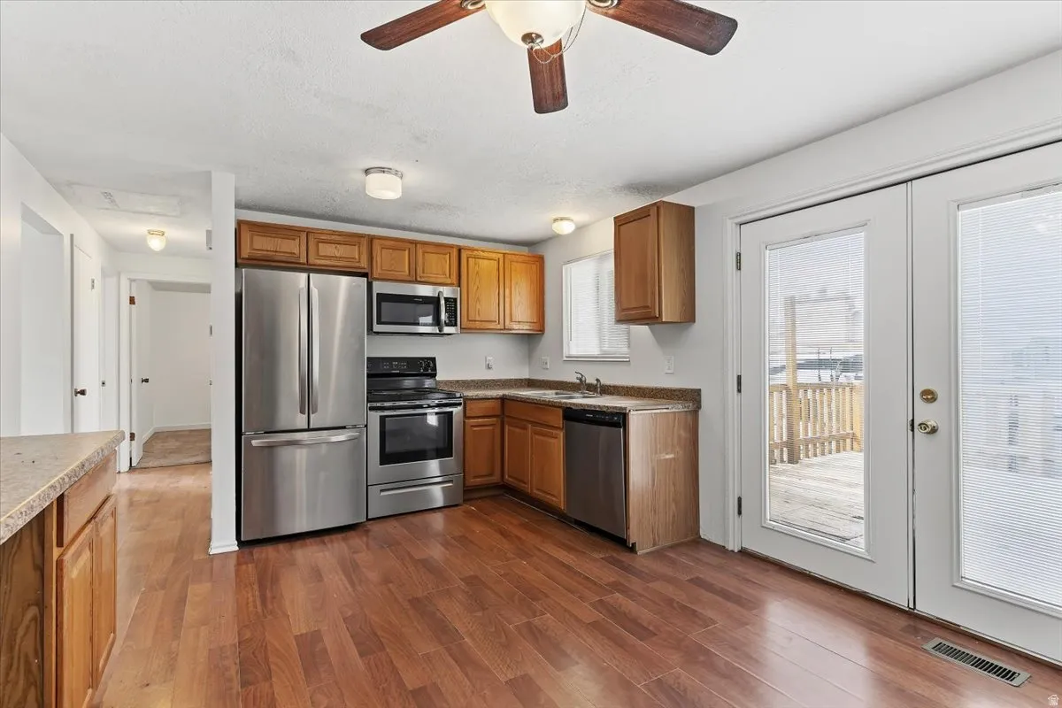 Kitchen with stainless steel appliances, wood finish cabinets, dark wood finished floors, ceiling fan, and french doors