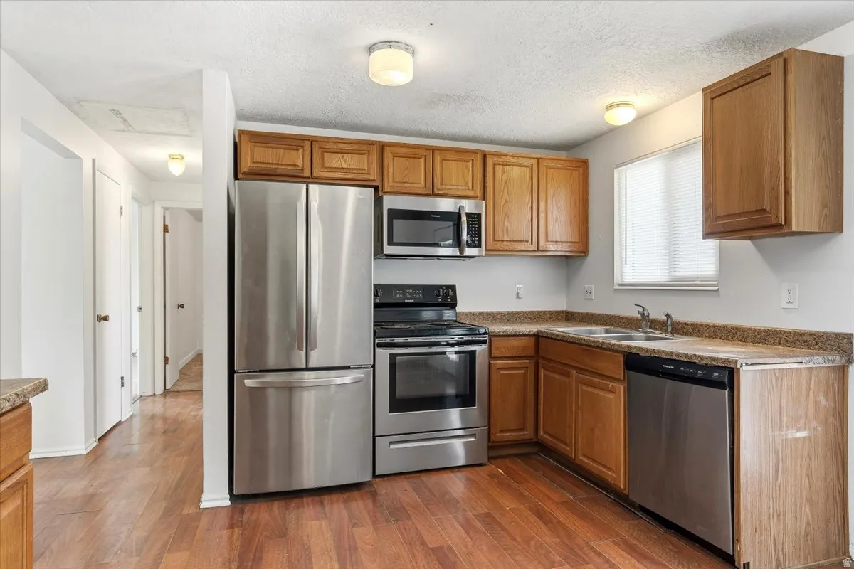 Kitchen featuring stainless steel appliances, a textured ceiling, dark wood finished floors, wood finish cabinetry, and dark countertops