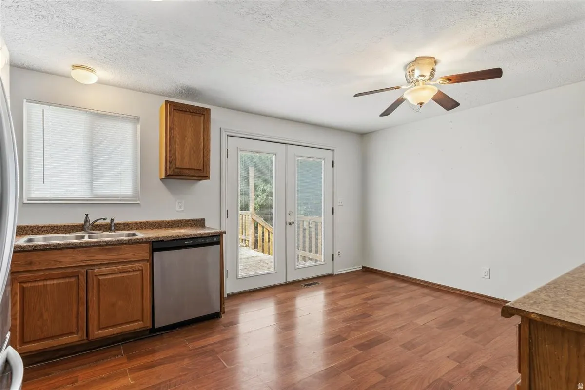 Kitchen featuring french doors, wood finish cabinets, dark countertops, a textured ceiling, and stainless steel dishwasher