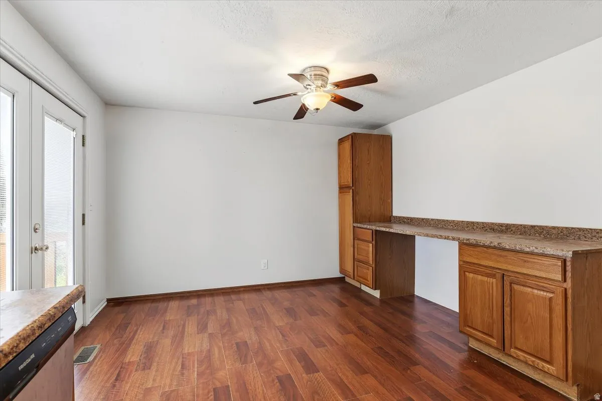 Unfurnished living room with built in desk, dark wood-style floors, a ceiling fan, and a textured ceiling