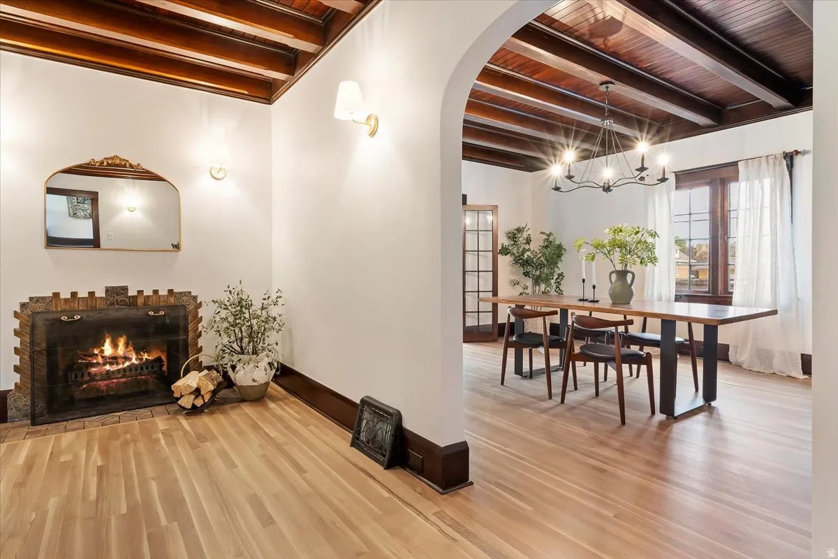 Hallway featuring arched walkways, hanging lights, light wood-type flooring, and a wooden ceiling with exposed beams