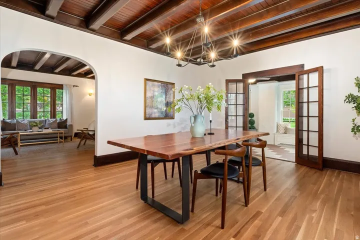 Dining area featuring french doors, a wooden ceiling with exposed beams, arched walkways, and light wood finished floors
