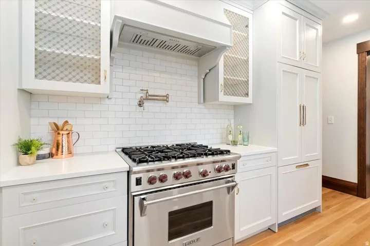 Kitchen featuring premium stove, white cabinets, light wood finished floors, backsplash, and light stone countertops