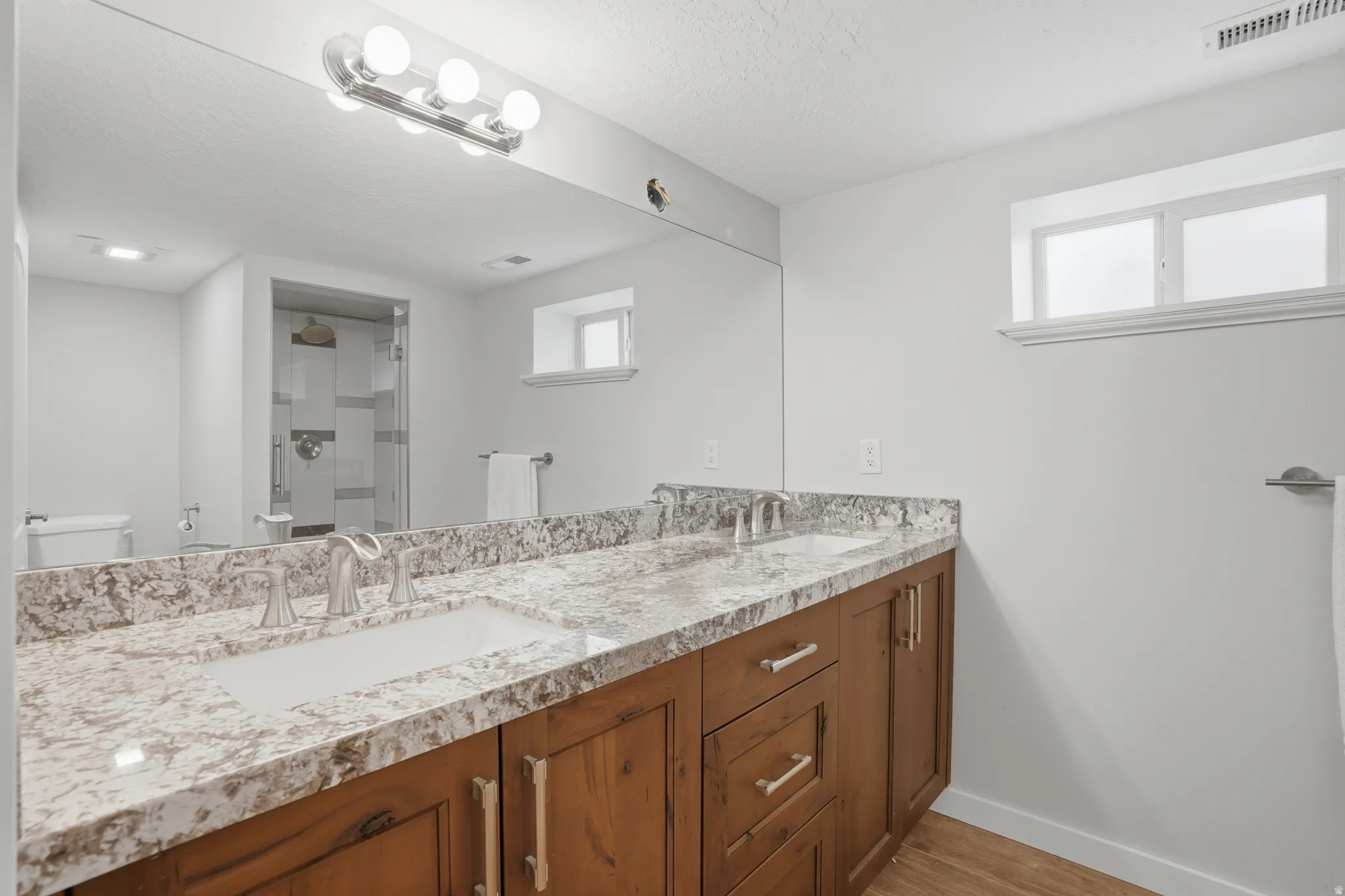 Bathroom featuring a stall shower, double vanity, light wood-style floors, and a textured ceiling