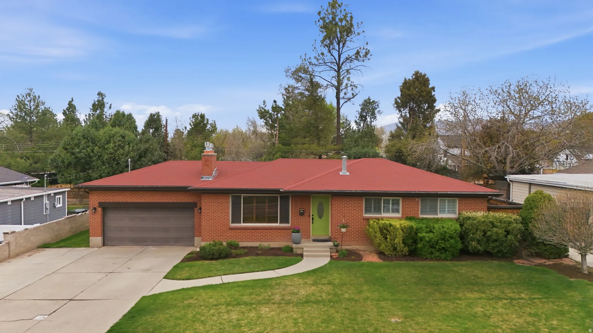 Rambler-style house with a garage, driveway, a chimney, a front yard, and brick siding