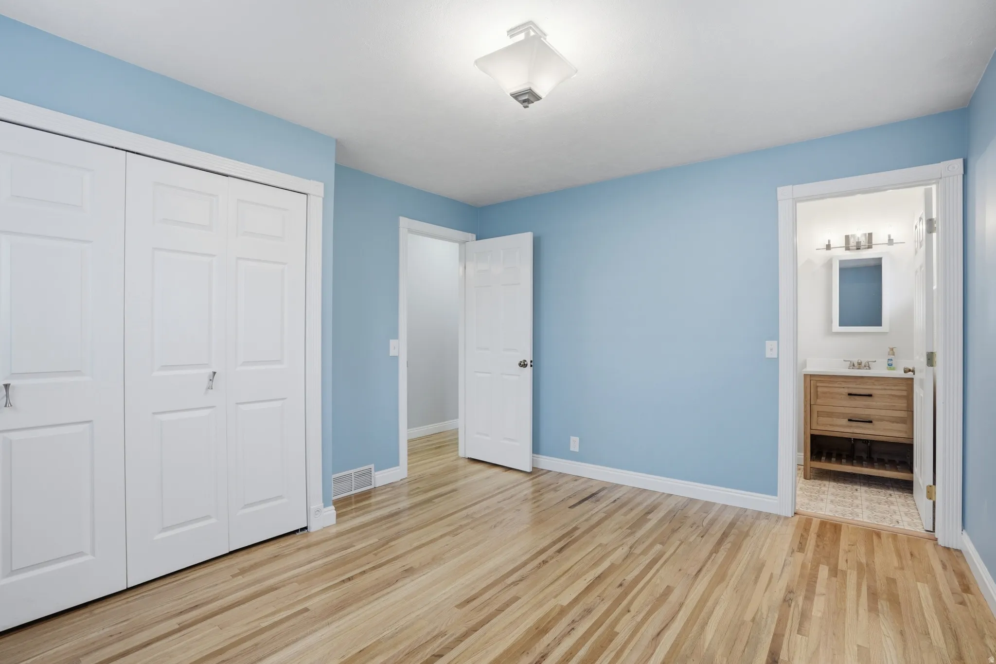 Unfurnished bedroom featuring a closet, light wood-style flooring, and ensuite bathroom