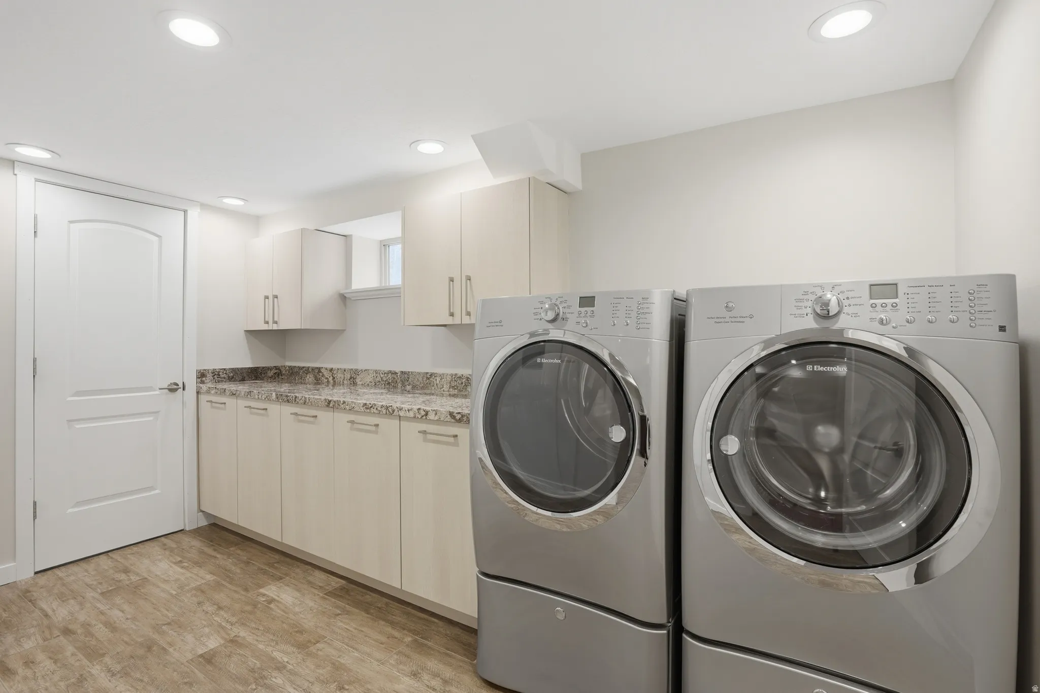 Laundry room with light wood-type flooring, washer and clothes dryer, recessed lighting, and cabinet space