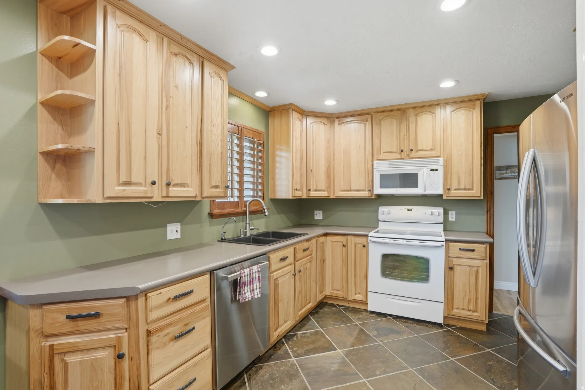 Kitchen with light wood finish cabinets, stainless steel appliances, open shelves, recessed lighting, and light countertops
