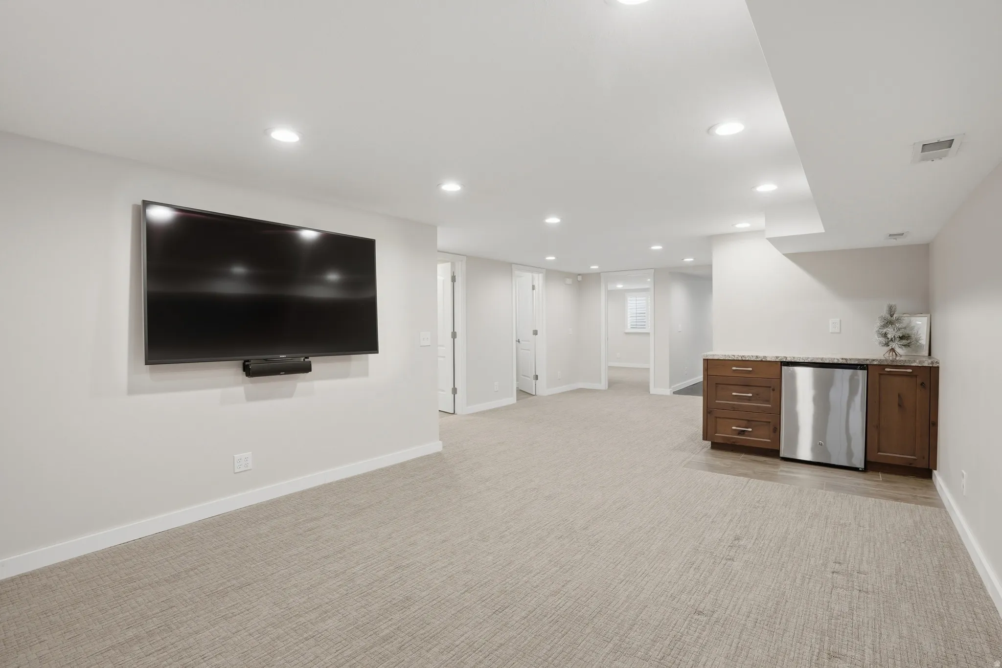 Bar featuring recessed lighting, light stone countertops, light colored carpet, stainless steel appliances, and dark wood finish cabinetry