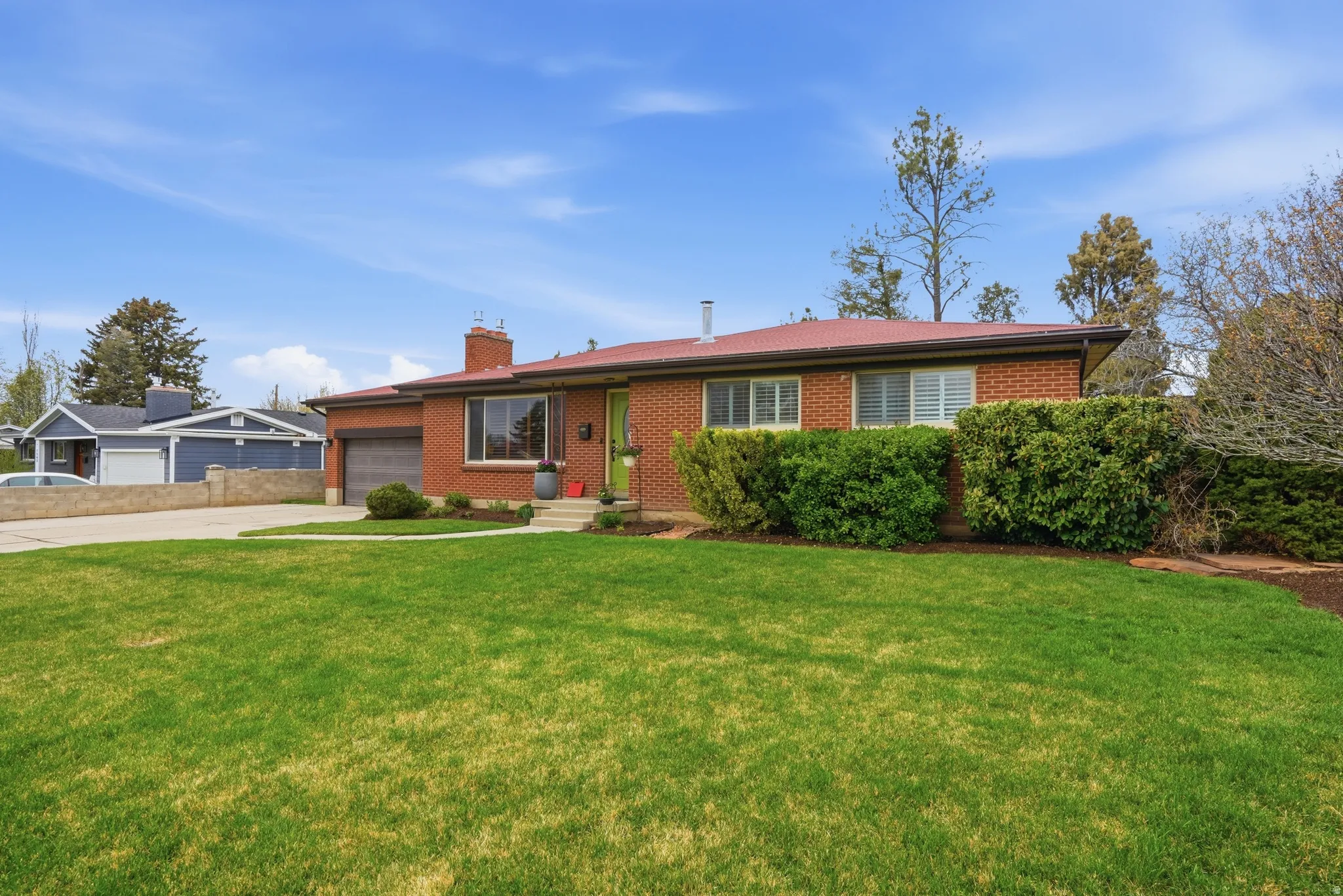 Rambler-style house with brick siding, a garage, a front lawn, driveway, and a chimney