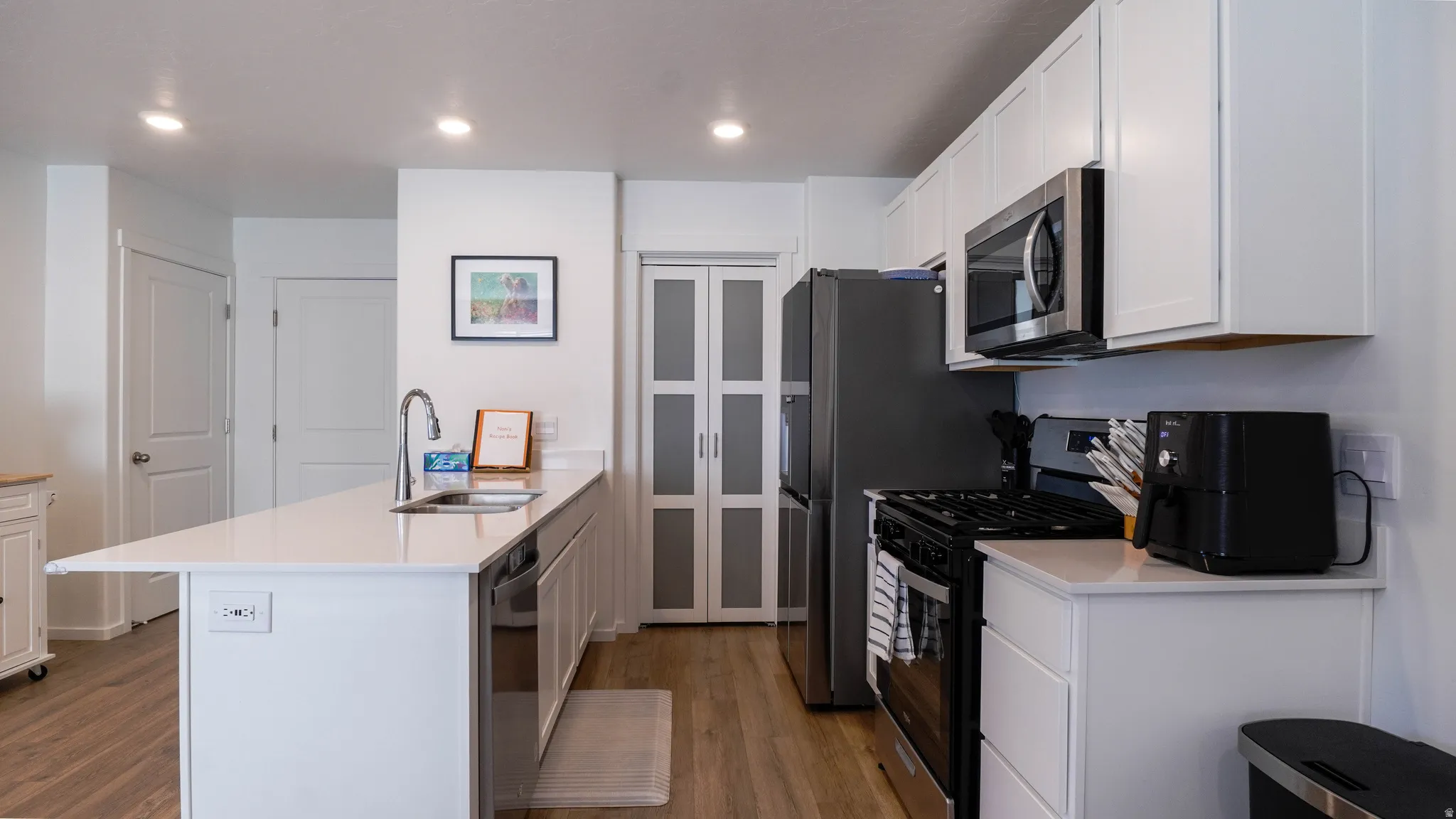 Kitchen with a peninsula, stainless steel appliances, white cabinetry, dark wood-style flooring, and light stone counters